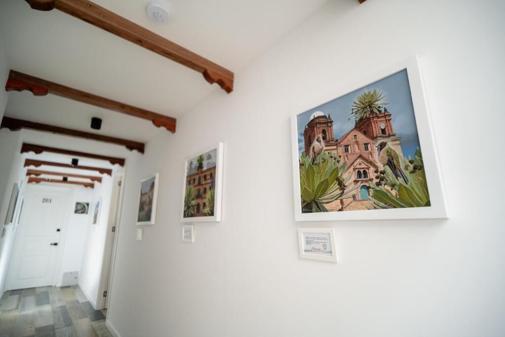 Un couloir orné de tableaux encadrés, avec des poutres en bois au plafond et une porte blanche portant le numéro 201.