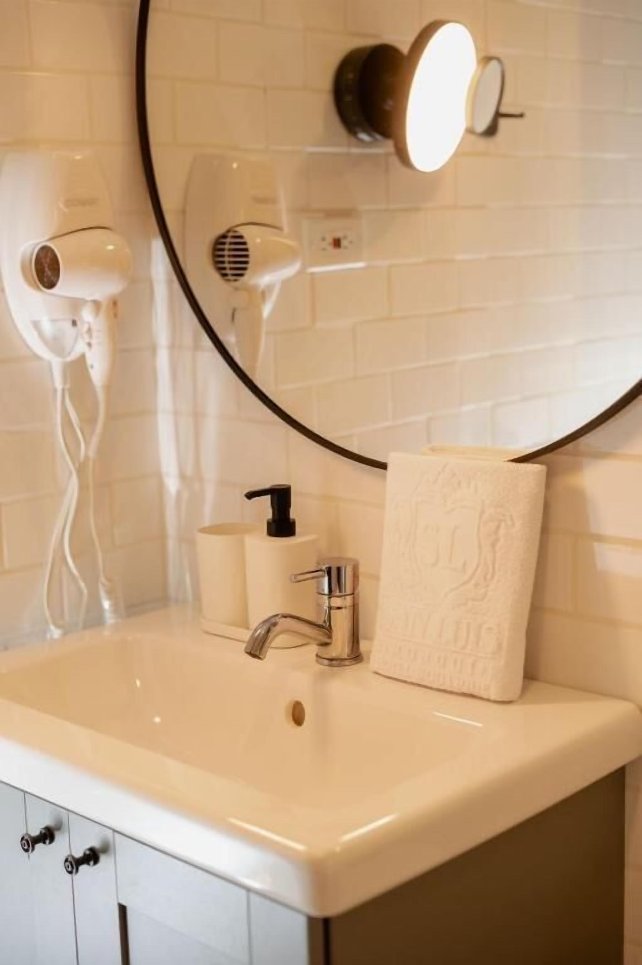 A bathroom with a white sink, a mirror with a black frame, and two hair dryers mounted on the wall.