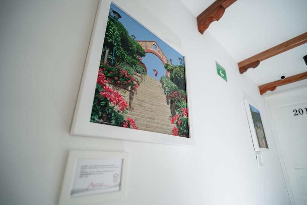 Un cuadro enmarco que muestra un jardín con un arco de ladrillo y flores rojas sobre una pared blanca.