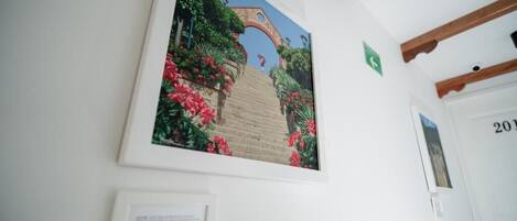 Un cuadro enmarco que muestra un jardín con un arco de ladrillo y flores rojas sobre una pared blanca.