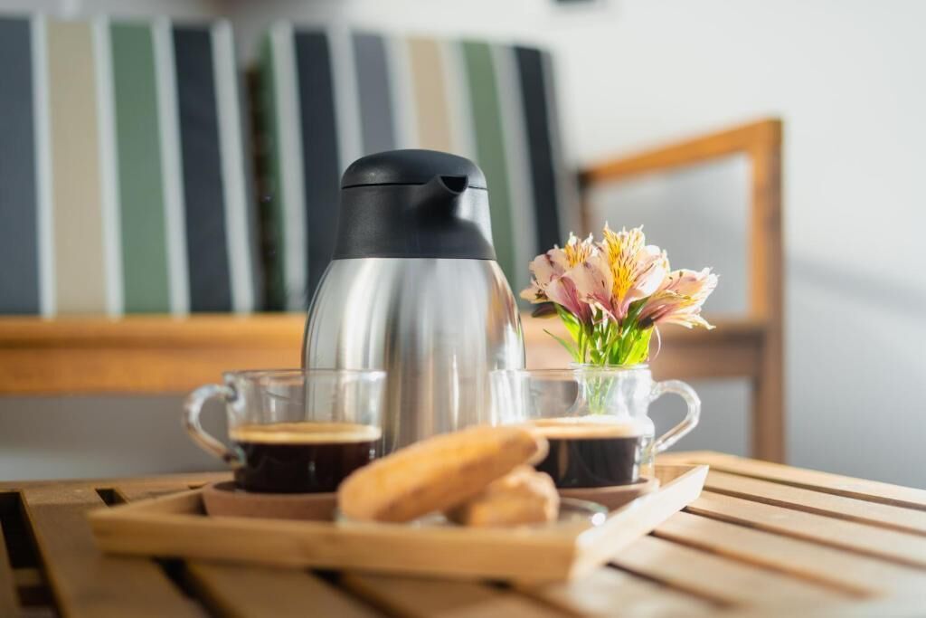 Eine Kaffeemaschine, eine Glaskanne, eine Blumenvase und ein Gebäckstück auf einem Holztisch.