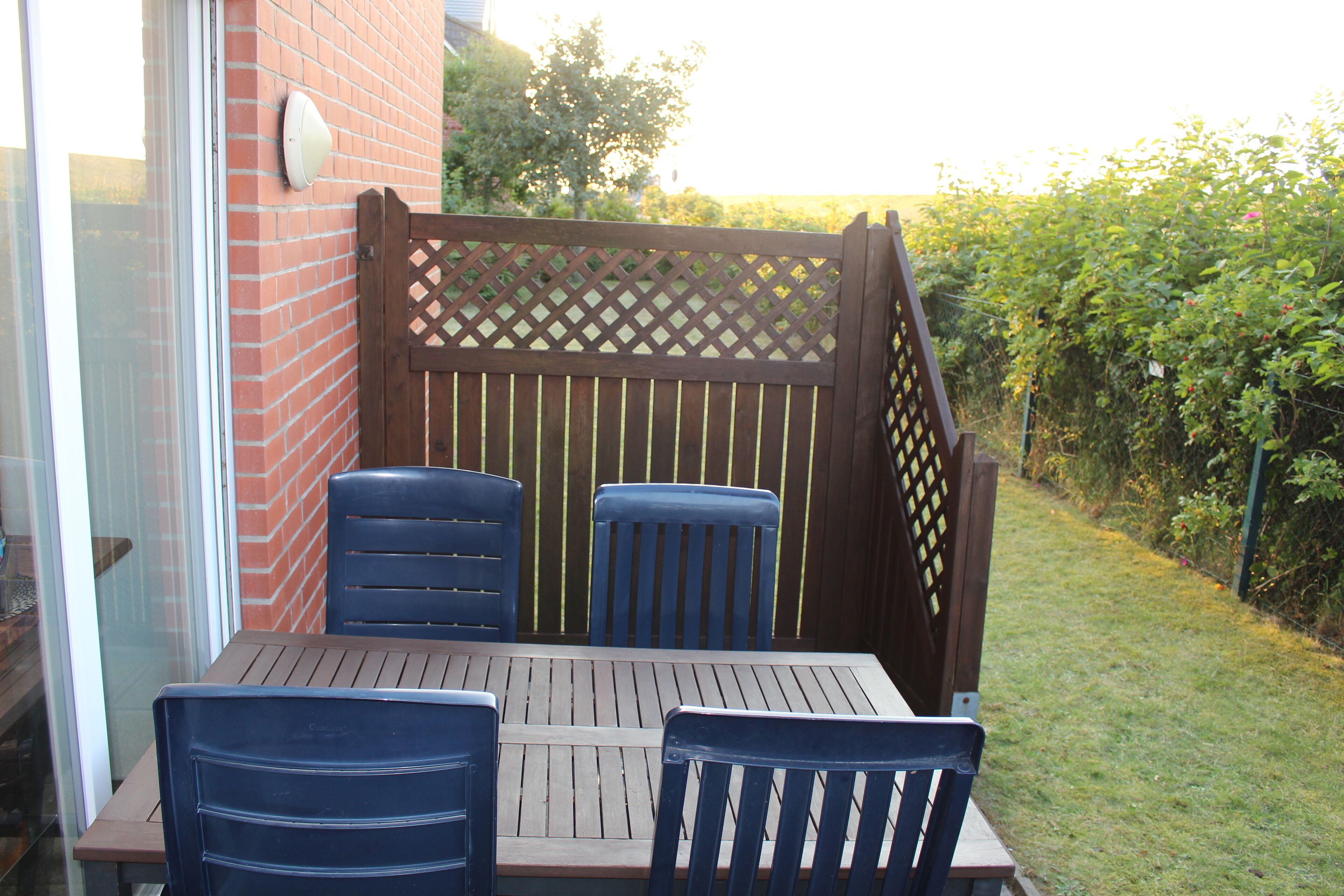 A patio with a table and four chairs, a wooden fence, and a brick wall.