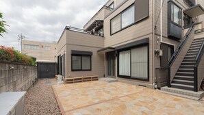 Un edificio residencial moderno con un patio de piedra, un pequeño jardín y una escalera que conduce a un nivel superior.