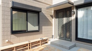 Fachada de edificio con tejas, un banco de madera y una puerta con reja de metal.