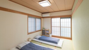 Una habitación tradicional japonesa con suelo de tatami, dos esteras de tatami, un bajo marco de cama de madera, un ventilador de techo y una puerta corredera estilo shoji.