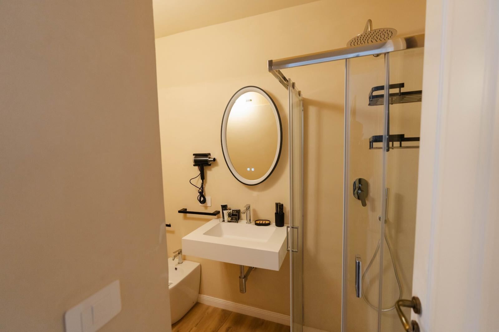 Un bagno con lavandino bianco, uno specchio, un asciugacapelli e cabina doccia in vetro.