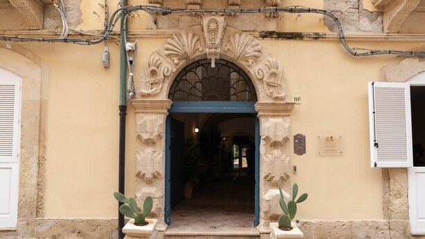 A building entrance with an ornate archway, a blue door, and two potted cacti. - Studio 1 apartment in Ortigia (Siracusa)