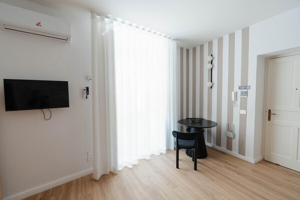A room with a flat-screen TV mounted on the wall, a round table with a chair, a door, and a striped wall.