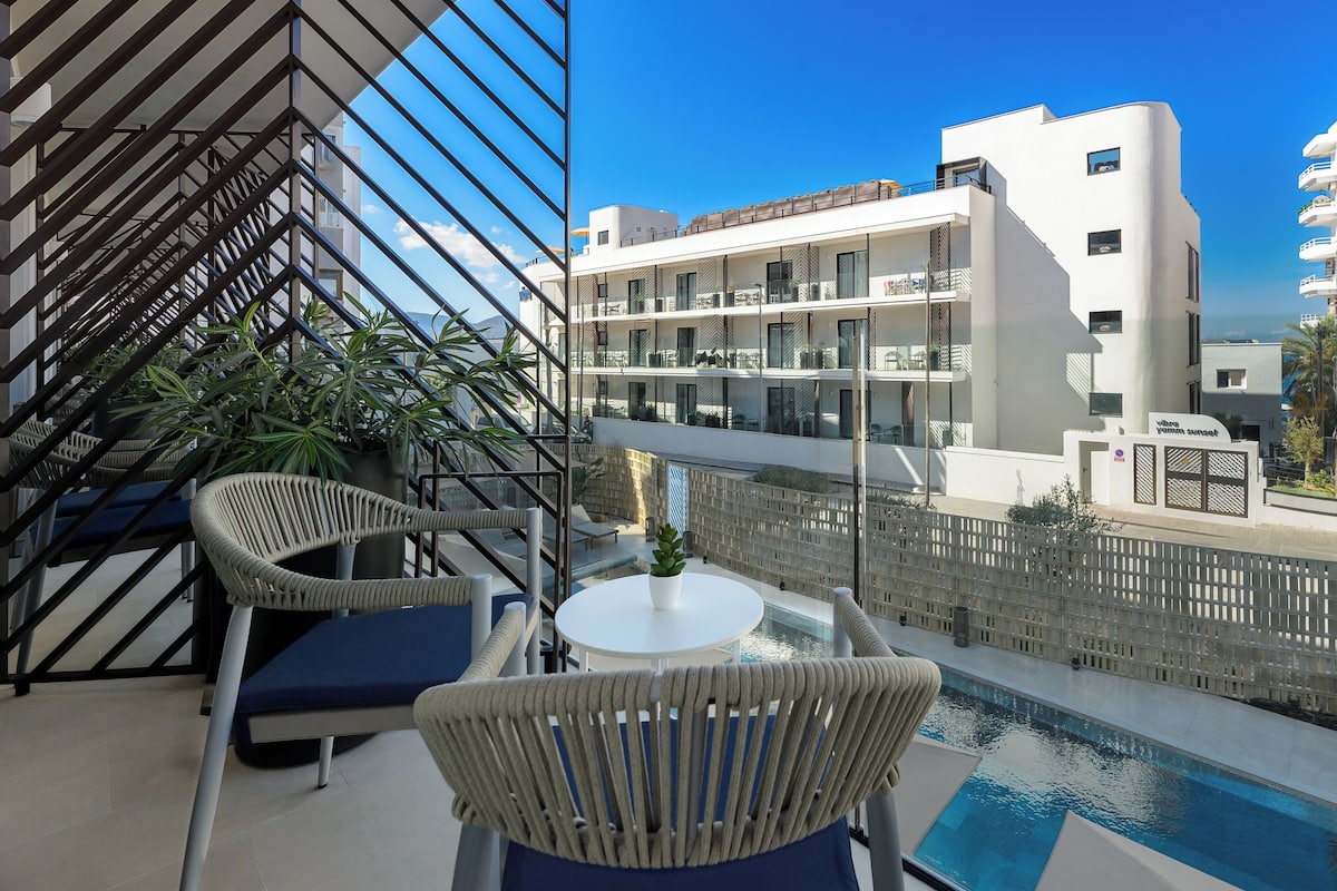 A balcony with wicker chairs, a small table, and a pool.