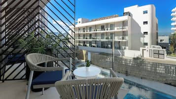 A balcony with wicker chairs, a small table, and a pool.