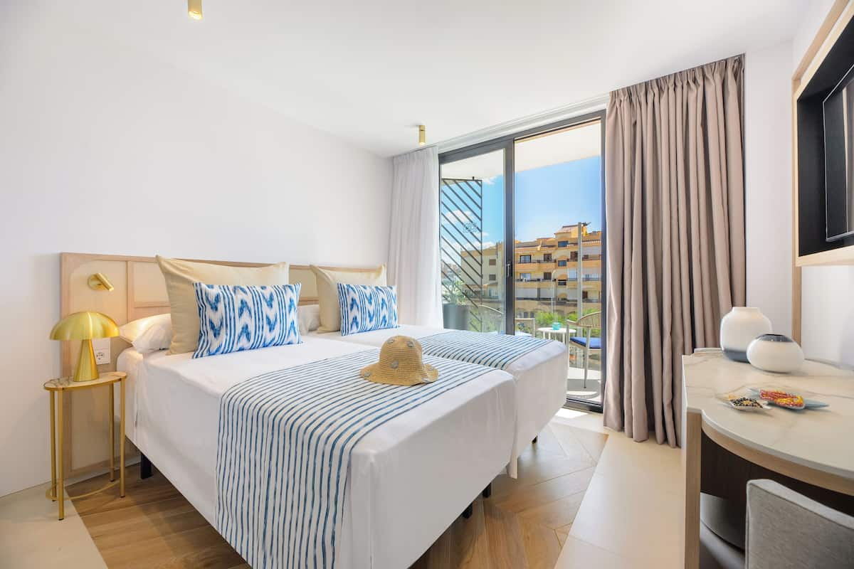 A hotel room with a large bed, a desk, and a view of buildings through the window.