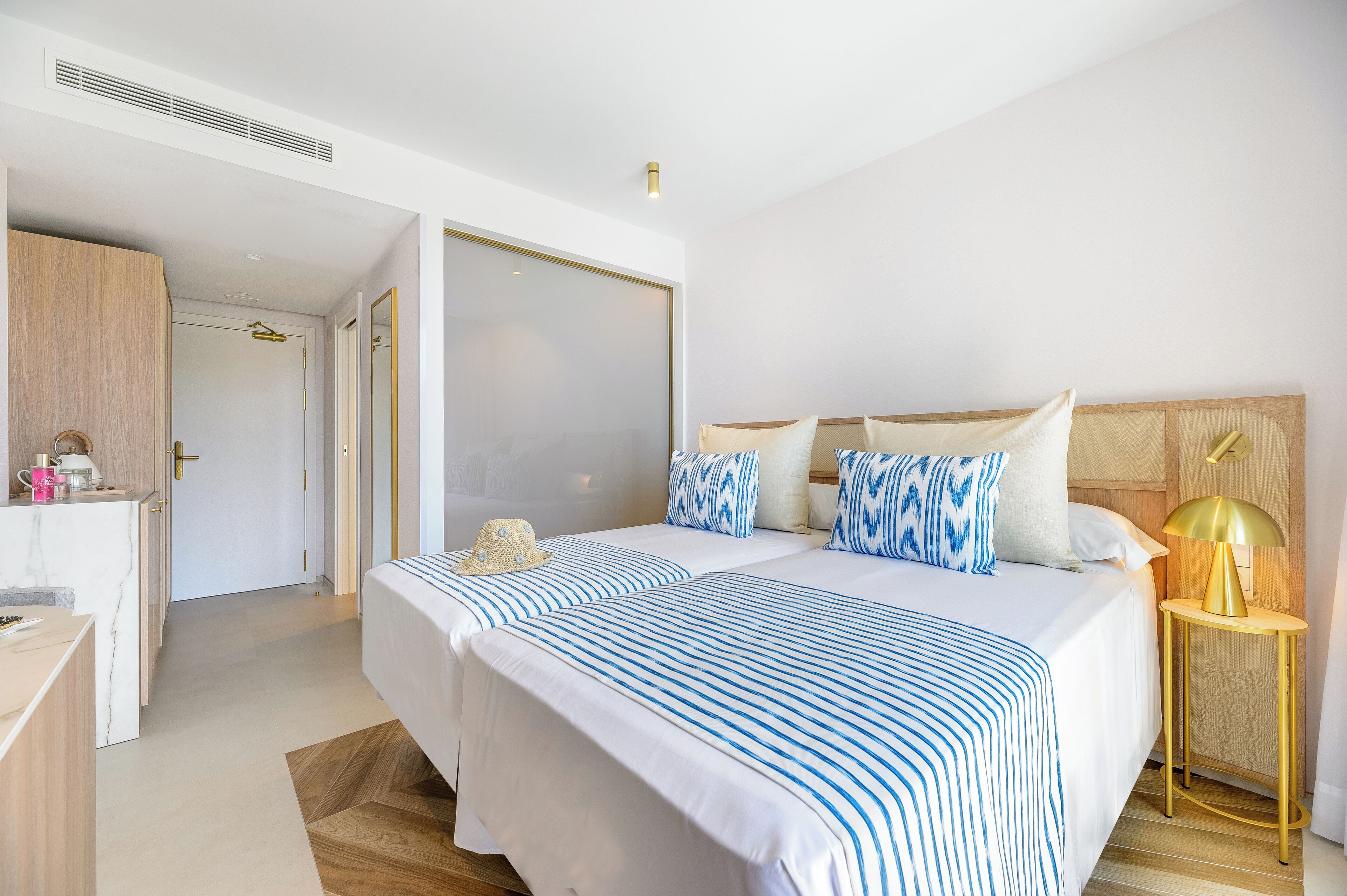 A hotel room with two beds, a desk, a wardrobe, and a bedside table with a lamp.
