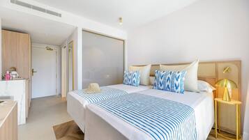 A hotel room with two beds, a desk, a wardrobe, and a bedside table with a lamp.