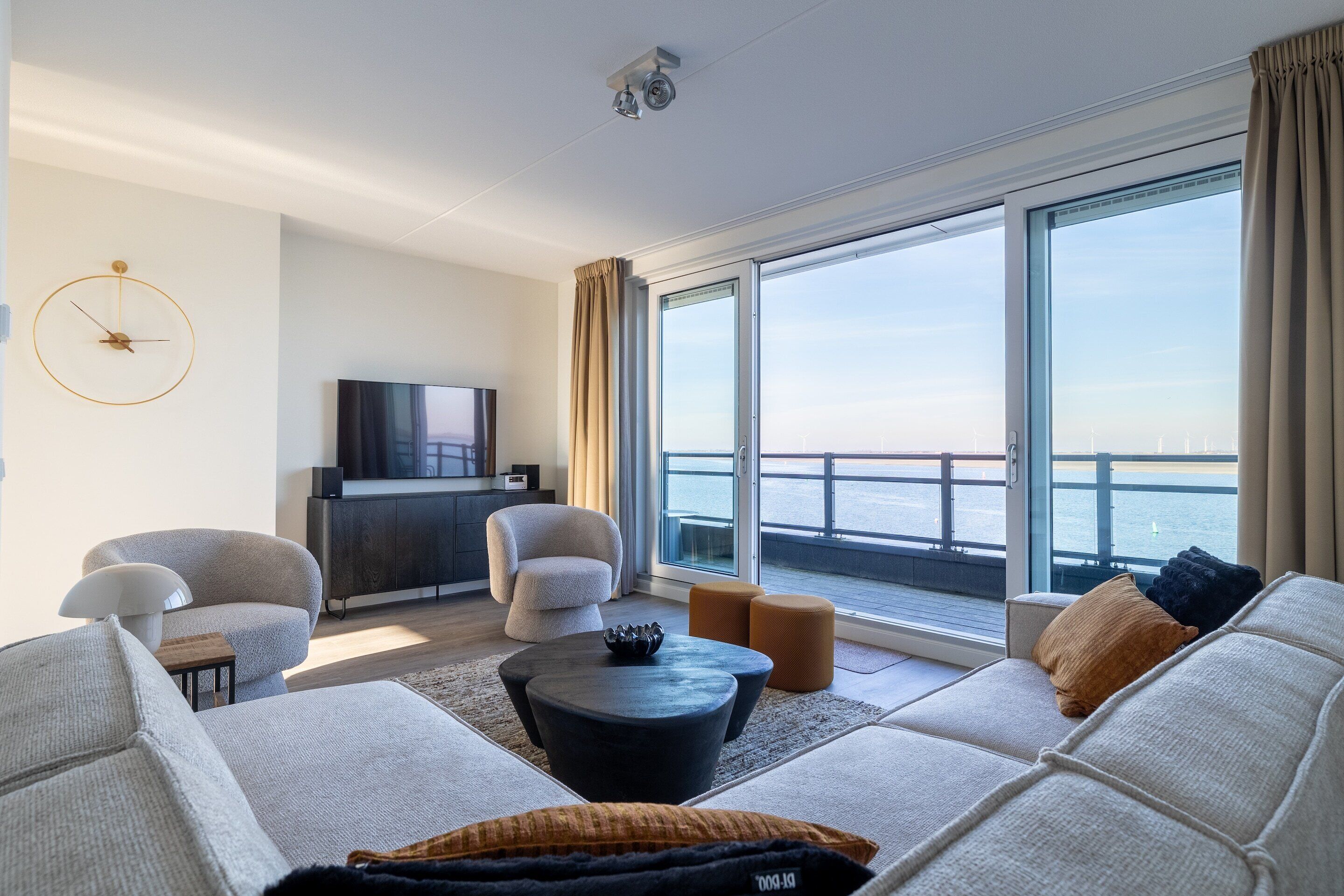 A modern living room with a sofa set, a coffee table, a TV, and a large window with a view of the sea.