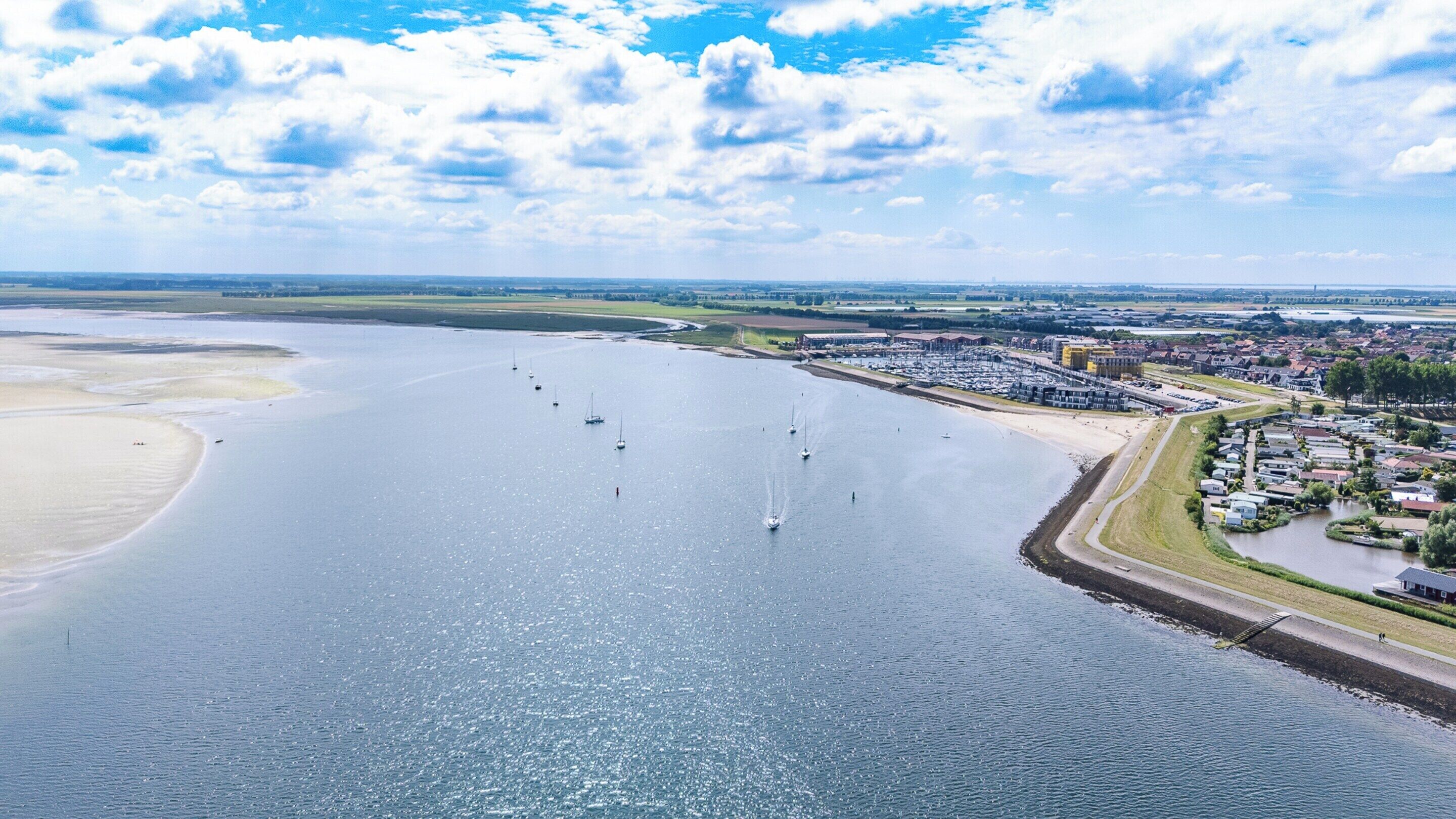 A coastal area with a marina, sandy beach, and a residential area with houses and buildings.