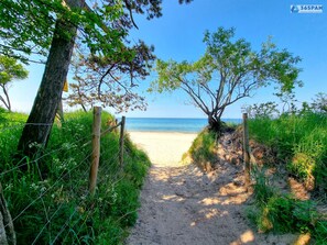 Ein sandiger Pfad führt zu einem Strand mit freiem Blick auf das Meer.
