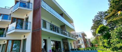 A modern multi-story residential building with balconies, large windows, and a well-maintained lawn.