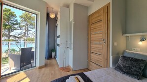 A bedroom with a bed, a wooden wardrobe, a balcony with wicker furniture, and a view of the sea. - Apartament Let's Sea 82 - 365PAM (Gaski)