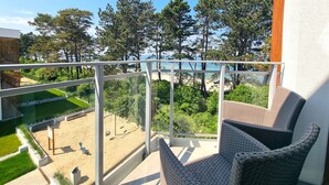 A balcony with a view of a beach, trees, and a swing set. - Apartament Let's Sea 82 - 365PAM (Gaski)