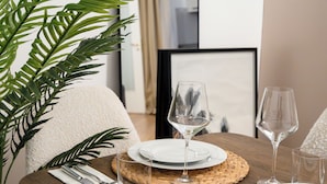 Une table à manger dressée avec de l’assiette blanche, des verres à vin transparents et un set de table en fibres tressées.