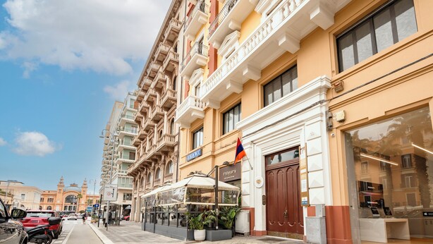 Un hôtel doté de nombreux balcons, un magasin avec un drapeau devant, et une vue sur la rue où sont garées des voitures.