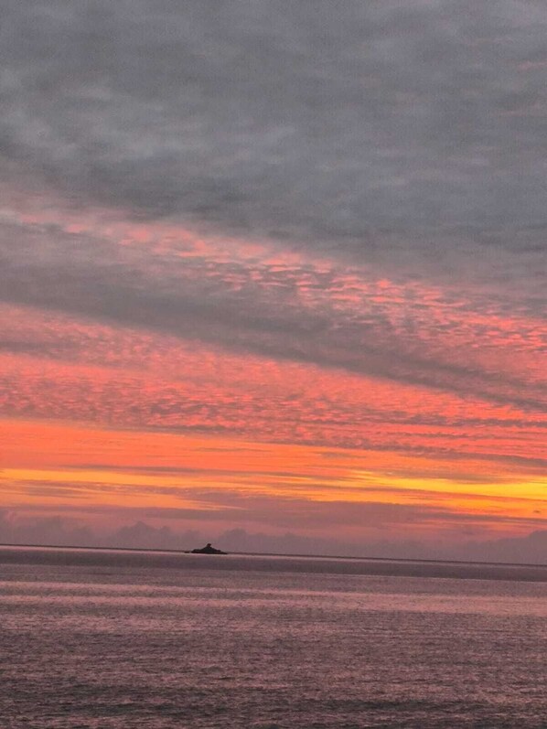 Un atardecer sobre un mar tranquilo con una pequeña isla a lo lejos.