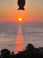 Atardecer sobre un mar tranquilo con siluetas de árboles y una casa en primer plano.