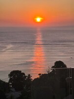 Atardecer sobre un mar tranquilo, con la silueta de árboles y un edificio en primer plano.