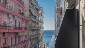 A narrow street with multi-story buildings, balconies, and a view of the sea.