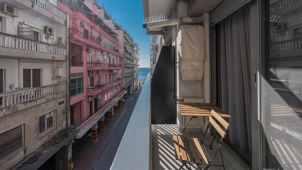 A narrow balcony with a view of a row of buildings and the sea.