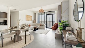 A modern living room with a dining area, a sofa, a coffee table, and a large window with a view. - Serene 2BR | Panoramic Sea View | Creek Edge | BMS (Dubai)