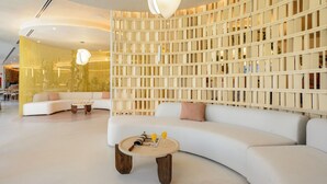 A modern interior with a curved white sofa, a round wooden coffee table with magazines and drinks, and a unique light fixture. - Hotel Vibra Yamm Sunset - Adults Only (Sant Antoni de Portmany)