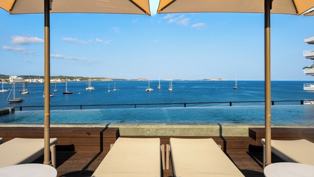 A poolside area with lounge chairs and umbrellas overlooking a marina with sailboats. - Hotel Vibra Yamm Sunset - Adults Only (Sant Antoni de Portmany)