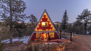 Une maison triangulaire à l’extérieur rouge, dotée d’un porche à l’avant et d’un escalier menant à l’entrée.