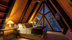 Une chambre confortable située dans les combles, avec un lit, des lampes de chevet, un logo Netflix et une vue sur les arbres à travers de grandes fenêtres.