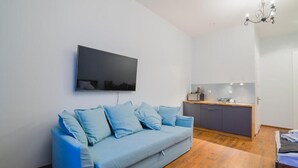 Una sala de estar moderna con un sofá azul claro, un televisor de pantalla plana montado en la pared y piso de madera.