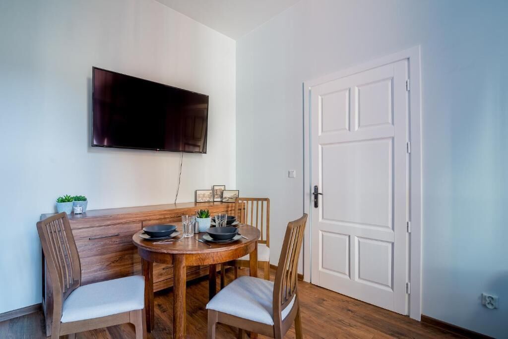 A dining area with a wooden table, four chairs, a flat-screen TV mounted on the wall, and a white door.