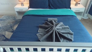 A neatly made bed with a teal bedspread and two pillows, a bedside table with a lamp, and a wall-mounted heater. - 4 Guests - Marina Point East Escape in Kent (Chatham)