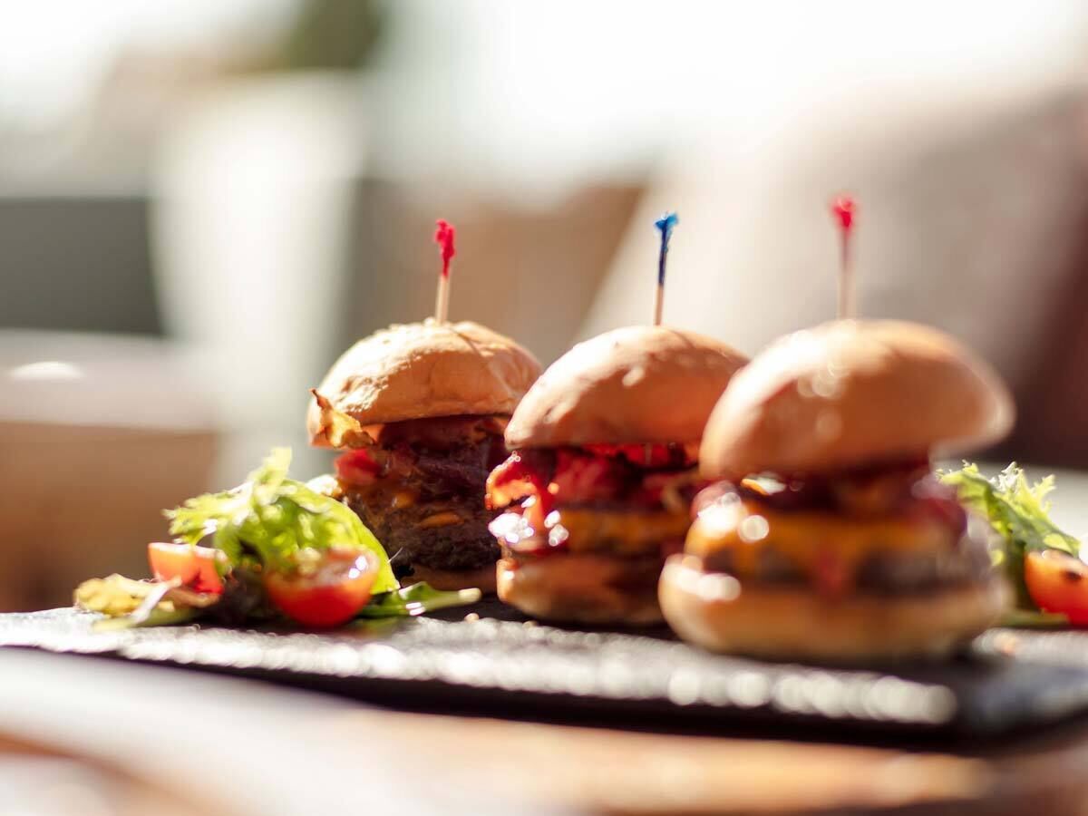 Trois hamburgers, maintenus ensemble par des cure-dents, sont présentés sur une assiette, accompagnés d’une salade.