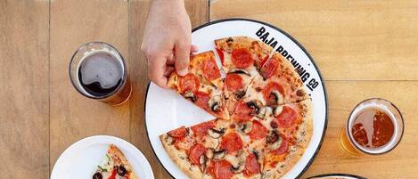 Una mesa de madera con porciones de pizza, una cerveza y un plato de comida.