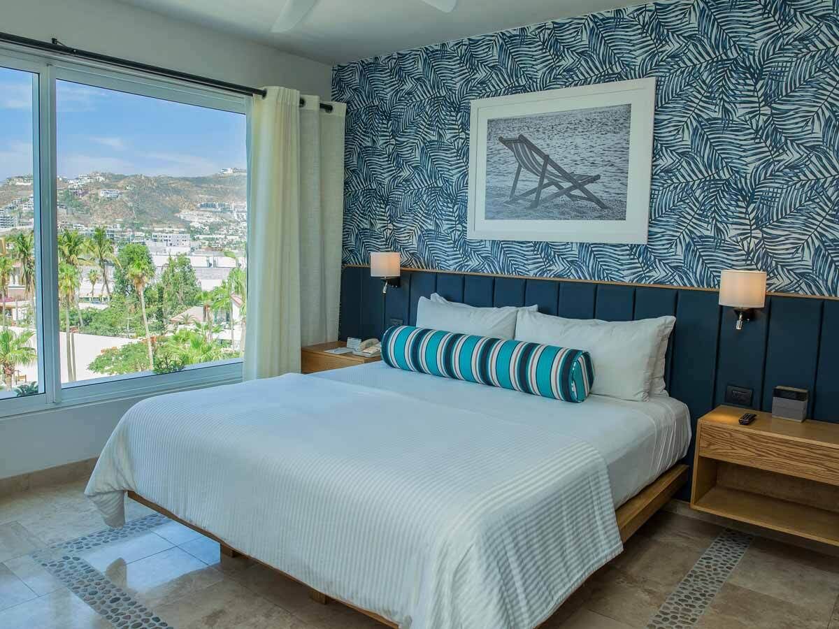 Une chambre d’hôtel avec un grand lit, une vue sur la ville et un papier peint aux motifs tropicaux.