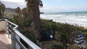 Vista costera con balcón que da al océano, palmeras y una silla de playa azul a rayas.