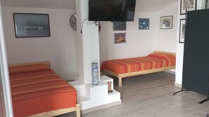Una habitación con dos camas individuales, un televisor fijado a la pared y varias fotografías enmarcadas.