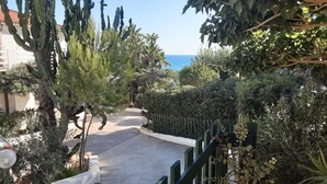 Un sendero bordeado por plantas y una cerca, que conduce a un edificio con vista al mar.