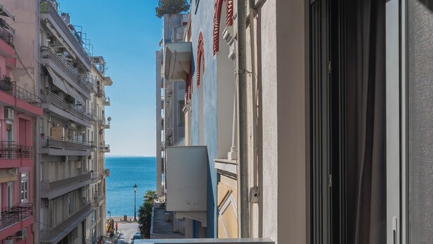 Une rue étroite, bordée de bâtiments des deux côtés, qui mène à un point de vue sur la mer.