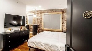 A modern bedroom with a large bed, a TV, a dresser, and a brick accent wall.