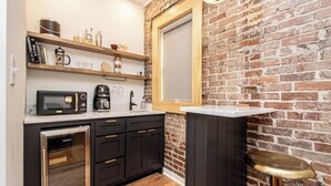 A compact kitchen with a brick wall, wooden shelves, a microwave, a coffee maker, and a small oven.