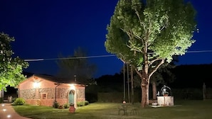 A house with a stone facade, a well-lit front door, and a large tree in the yard. - L'OCA GIULIVA RELAIS  (Gaggio Montano)