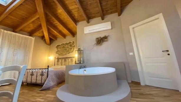 A bathroom with a freestanding bathtub, wooden beams, a stone wall decoration, and a door. - L'OCA GIULIVA RELAIS  (Gaggio Montano)