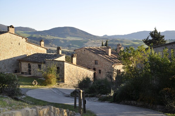 A stone building with a tiled roof, surrounded by greenery and hills in the background. - 2-bedroom rustic apartment in charming Gambassi with WiFi (Gambassi)